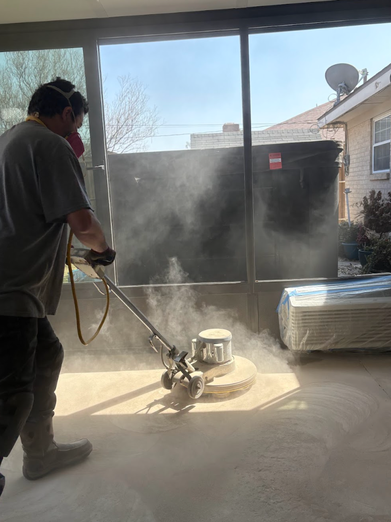 A person uses a floor buffer on a concrete patio, creating a large cloud of dust.