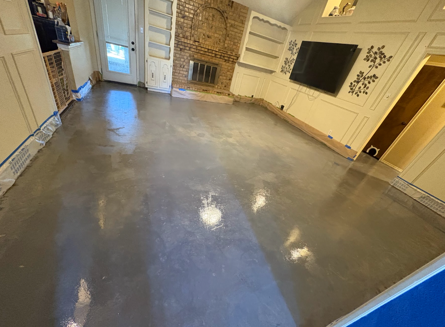 A recently finished room with polished grey concrete floors, white walls, built-in shelves, and a wall-mounted TV.
