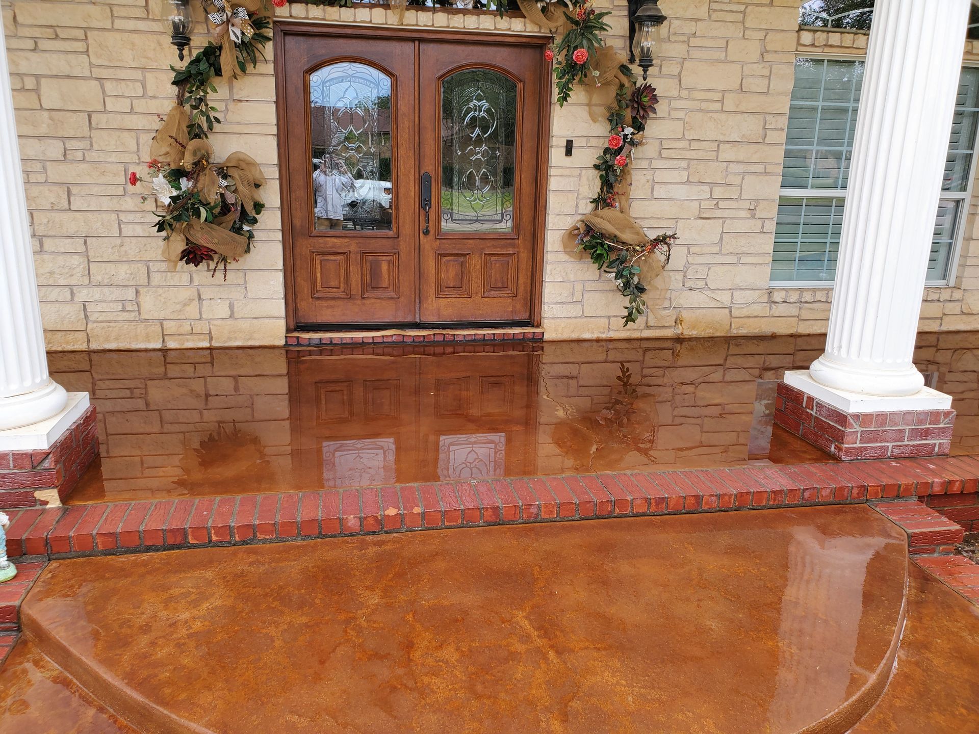 Exterior of a house with brown front doors, columns, and a reddish-brown porch. Decorations are above the doors.