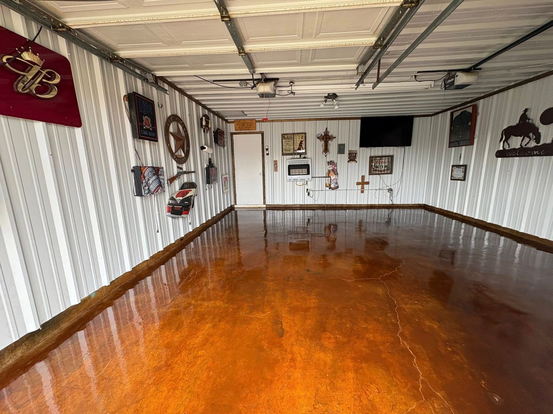 Shiny copper-colored garage floor. Walls have decor including a Budweiser banner, clocks, and crosses.