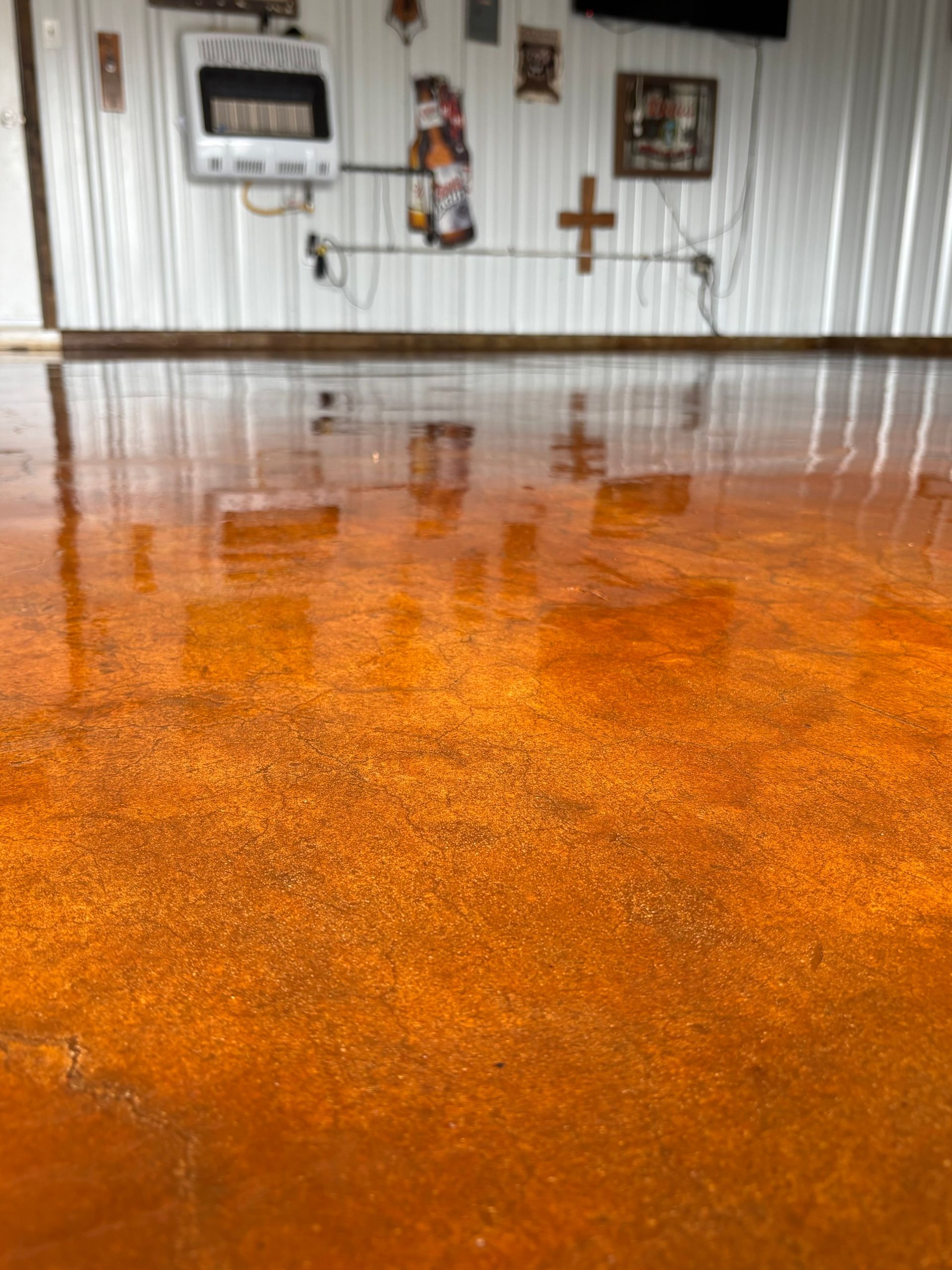 Orange, glossy, stained concrete floor reflecting a white-walled room with décor.