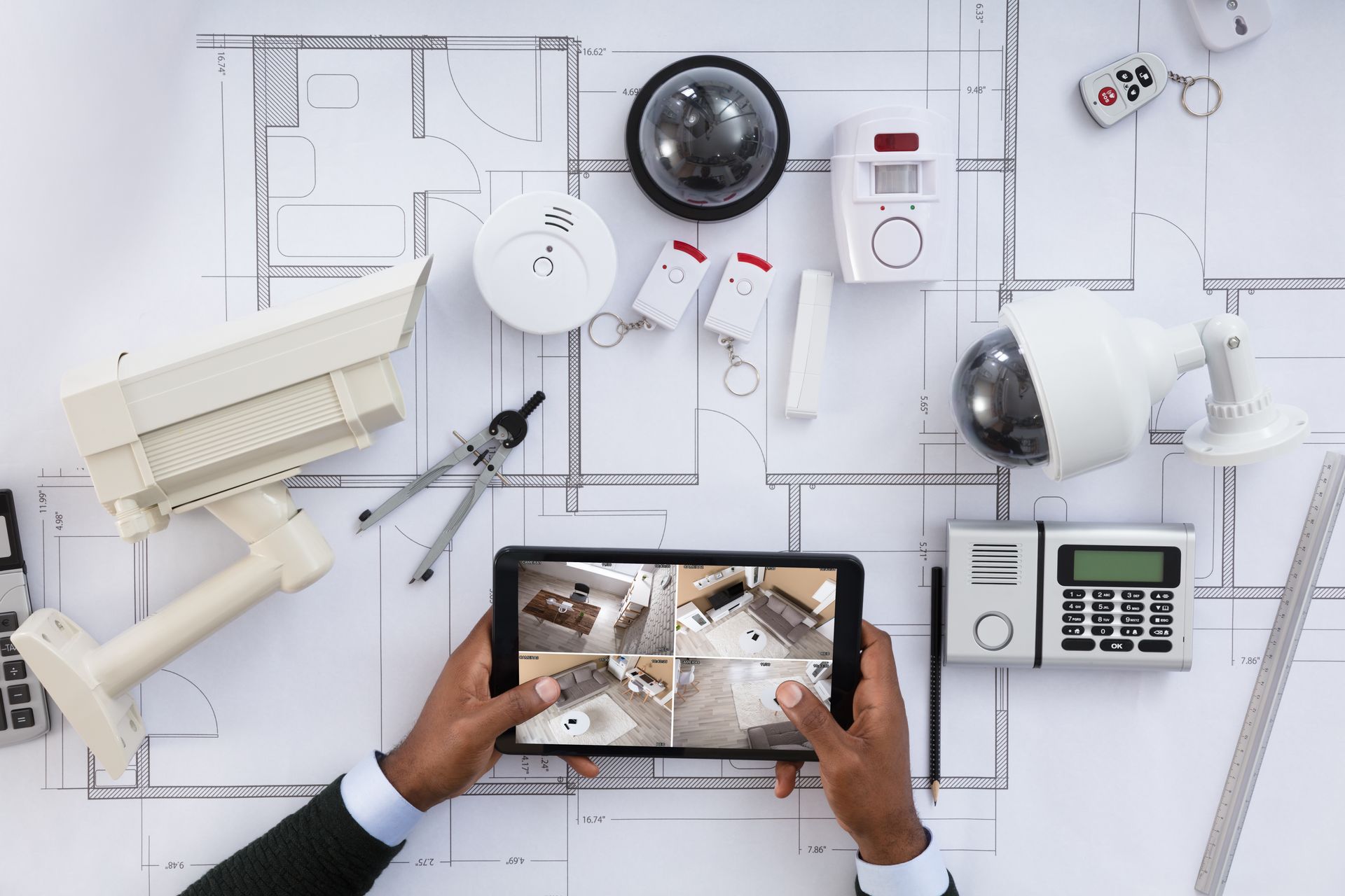 Smart home security devices on floor plan with tablet showing CCTV feeds.