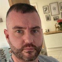 Man with short hair and beard, looking at the camera, indoors.