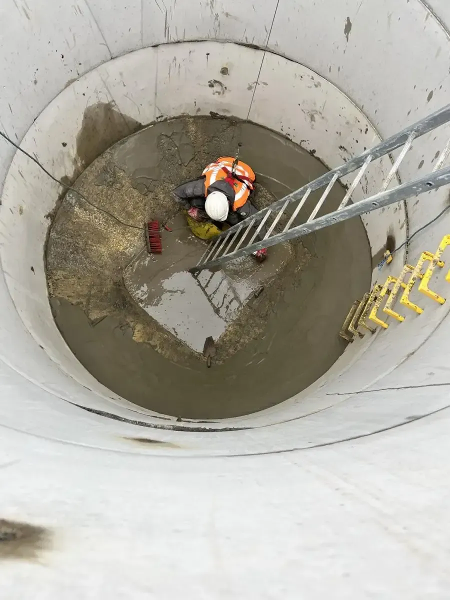 Person in safety gear working inside a large concrete cylinder with a ladder.