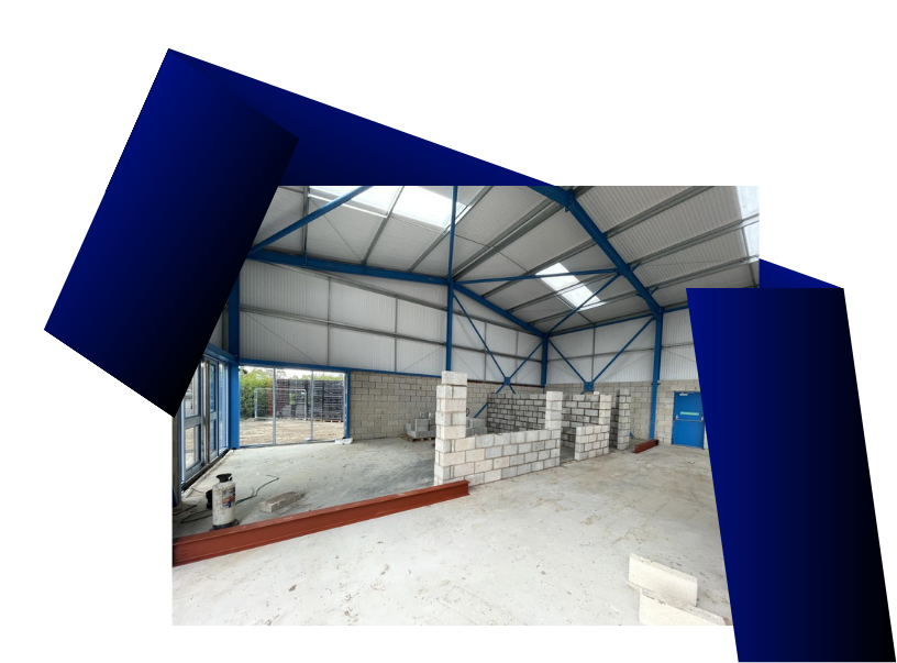 Interior of a large, empty warehouse under construction with blue structural beams and a partially built wall.