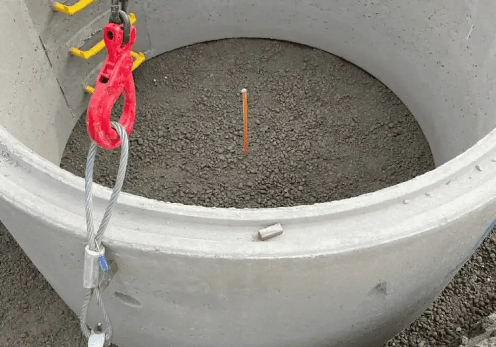 Concrete cylinder with gravel fill, hook and cable overhead, pencil, and small object inside.