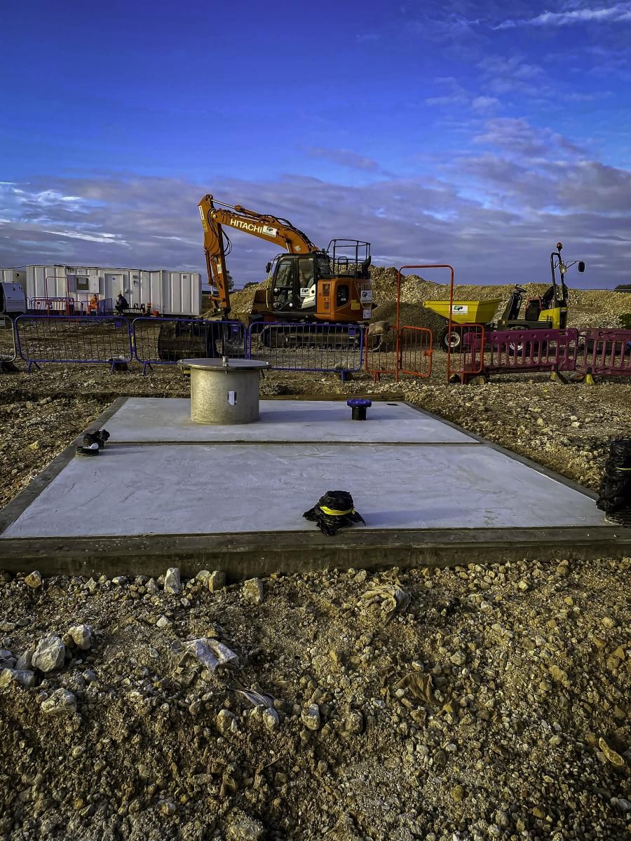 Construction site: excavator and concrete slab with a circular pipe, against a cloudy blue sky.