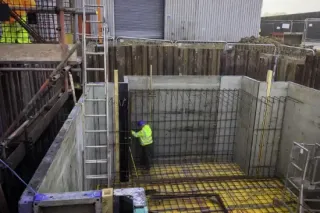 Construction worker inside a concrete pit assembling metal rebar framework. 
