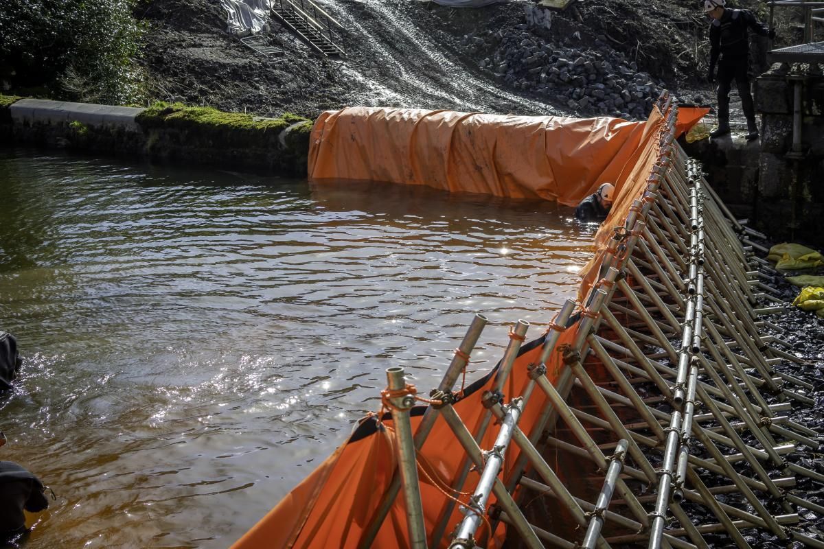 Orange barrier in a waterway, possibly for erosion control. Bamboo supports frame, water flowing.