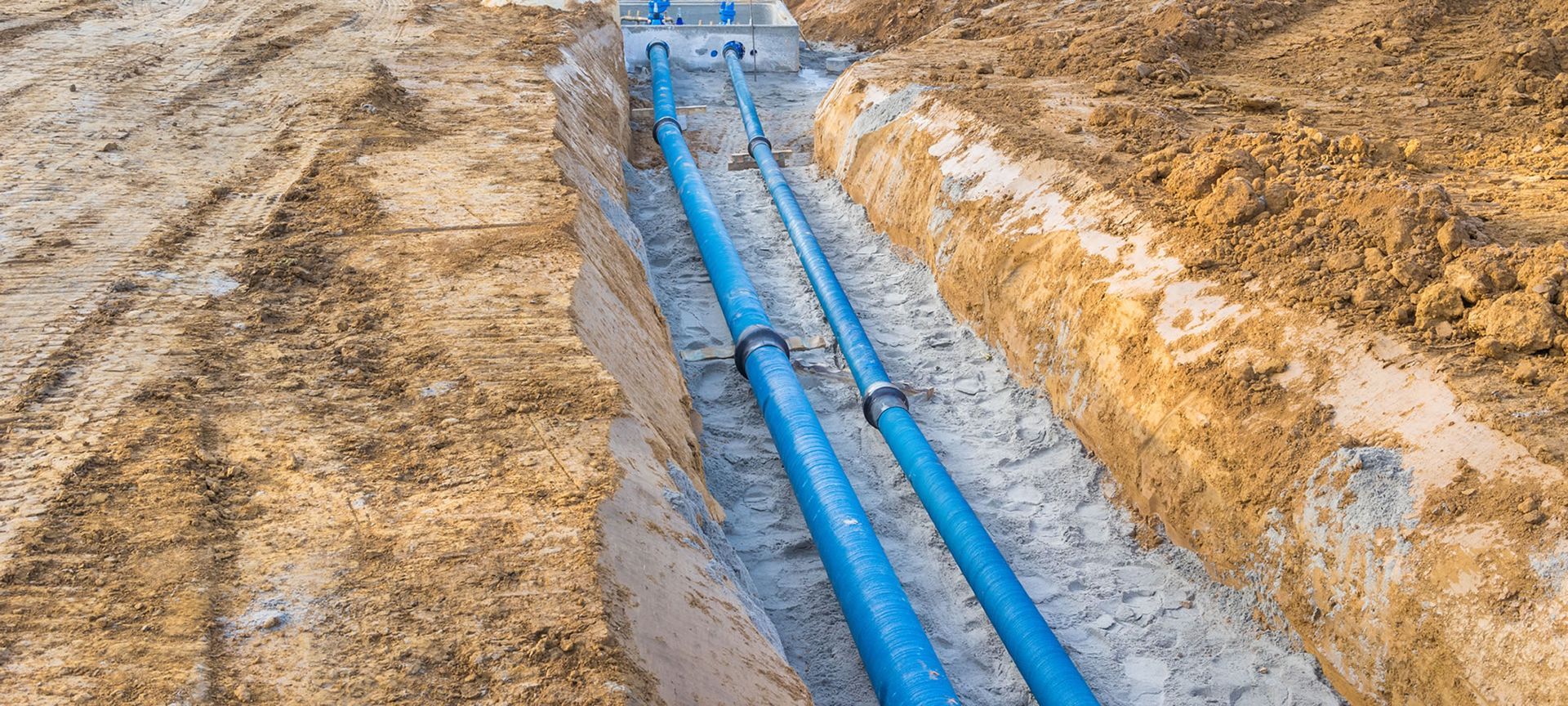 Blue pipes laid in a trench, next to brown soil. Construction site.