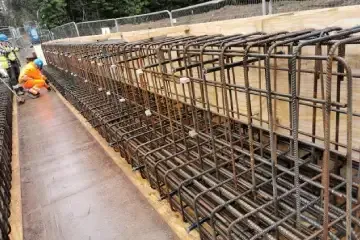 Reinforced steel bars in a rectangular formwork, construction site. Two workers in the background.