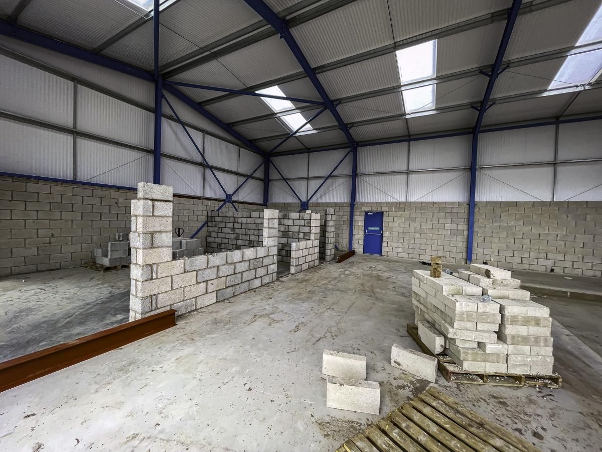 Interior of an industrial warehouse under construction, with block walls, a blue door, and stacked concrete blocks.