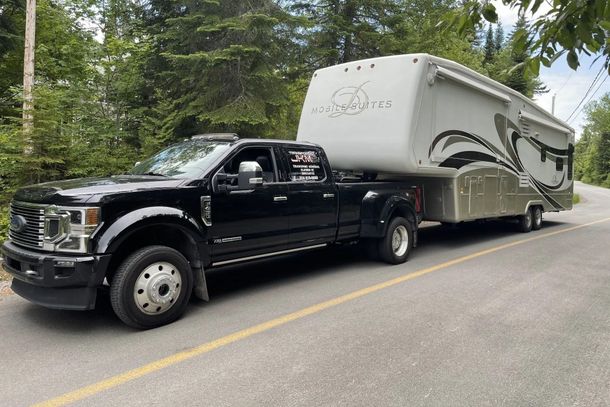 Un camion noir tracte une grande caravane à sellette sur une route sinueuse bordée d'arbres.