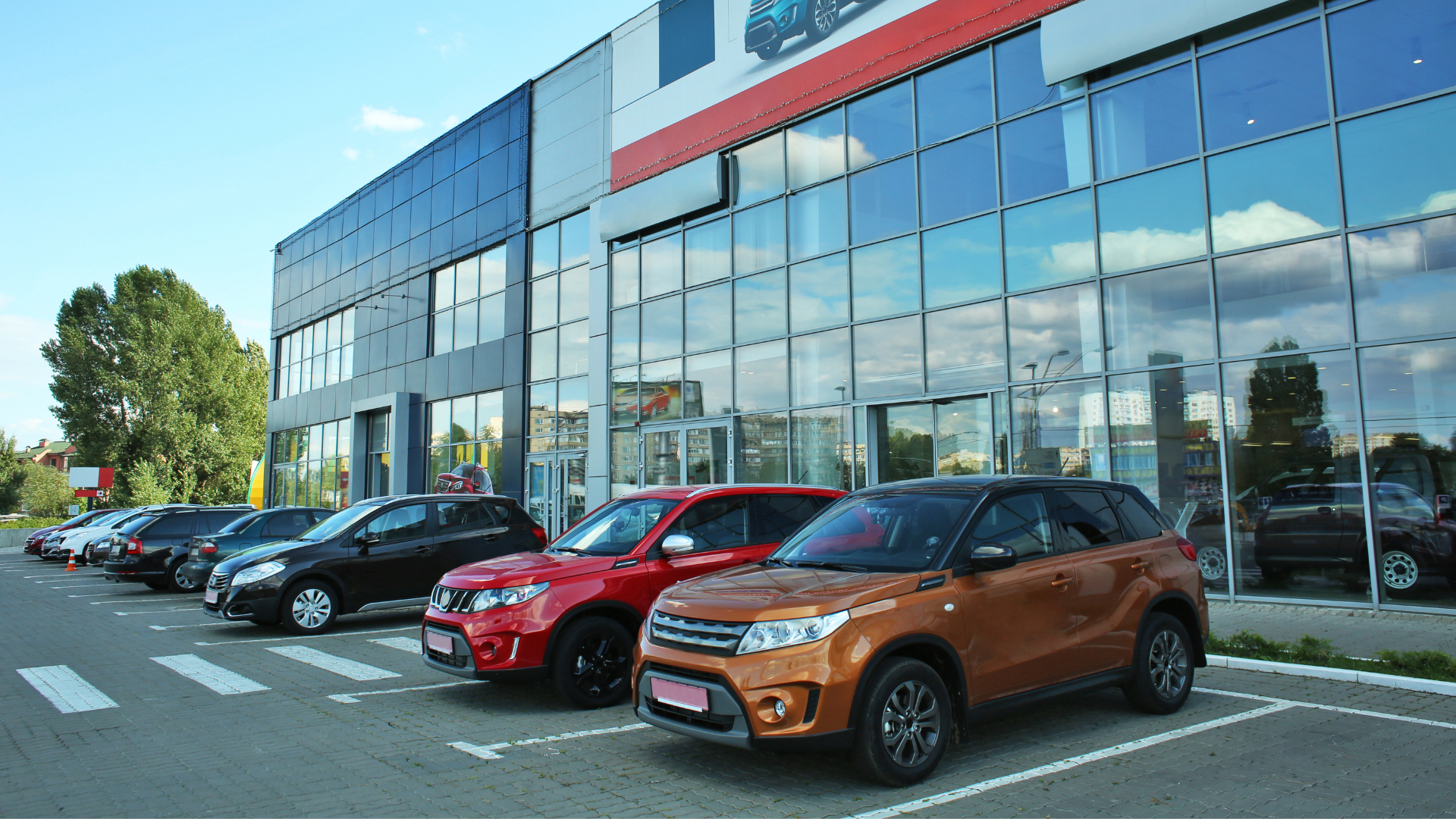 A row of cars are parked in front of a car dealership.