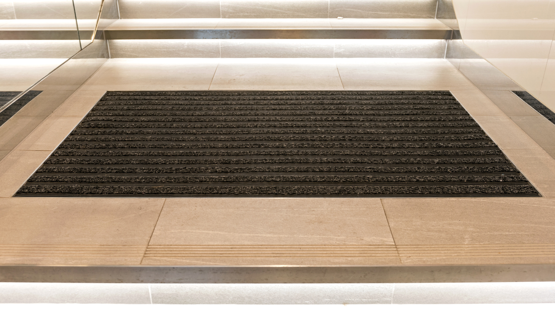 A black mat is on the floor of an elevator.