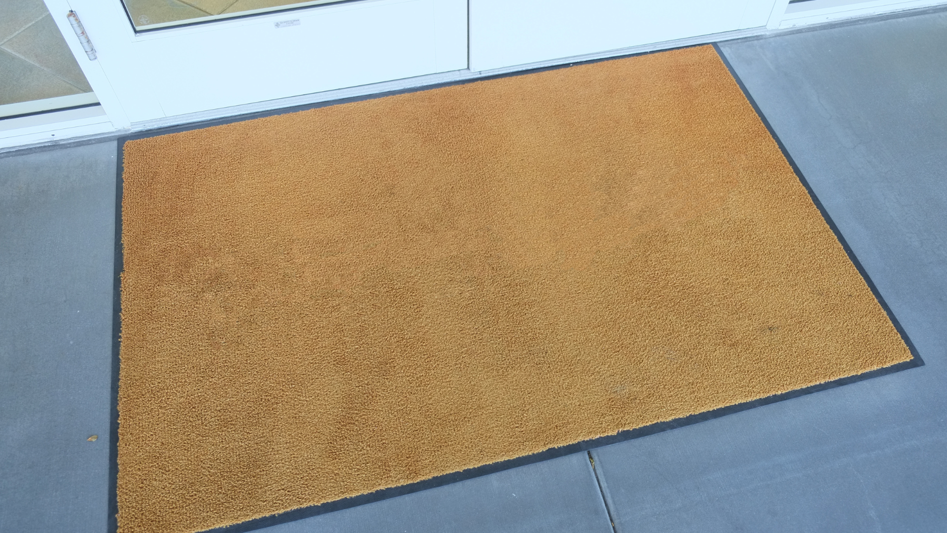 A brown door mat is sitting on a concrete floor in front of a door.