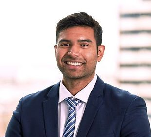 Woman in red blazer smiles, indoors, chest-up view.