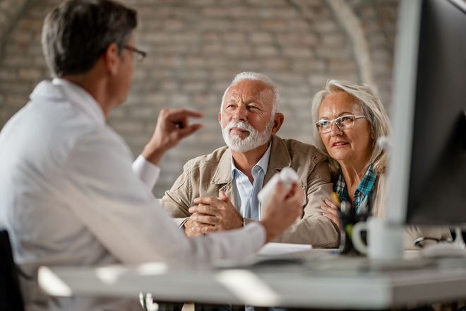 Doctor speaking with an elderly couple at a table in a bright office