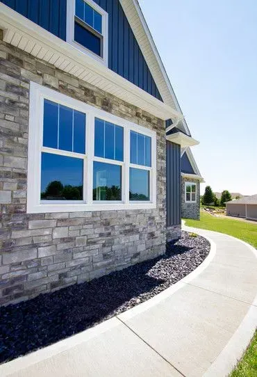 House exterior with stone and blue siding, white-framed windows, and a curved sidewalk.