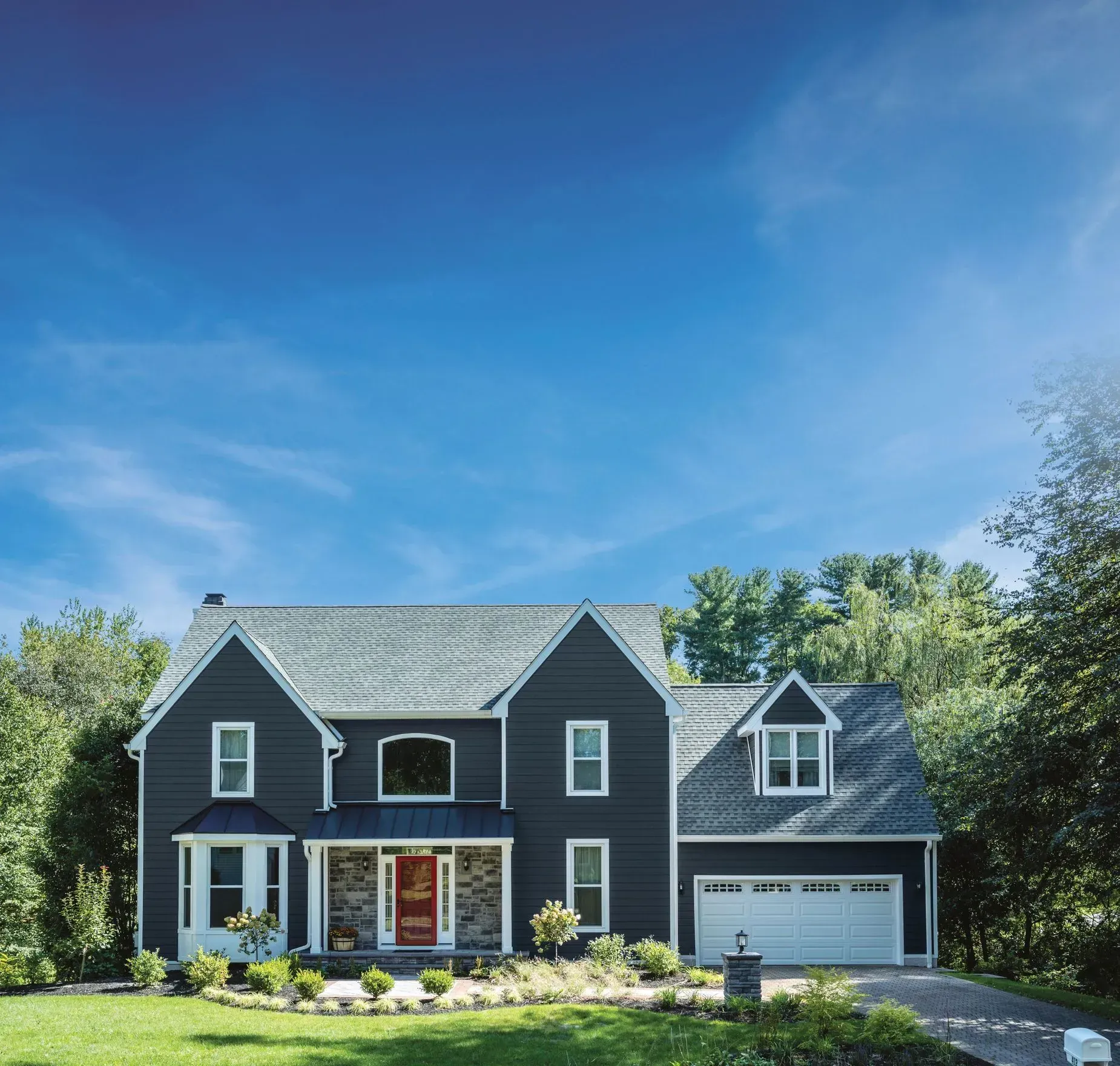 Two-story blue house with red door and white trim under a blue sky.
