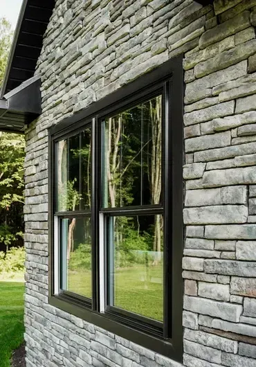 Window with black frame set in a stone wall, reflecting a green landscape.