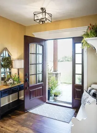 Open entryway with maroon door, rug, and view to outdoors. Yellow walls, dark furniture, and a bright view.