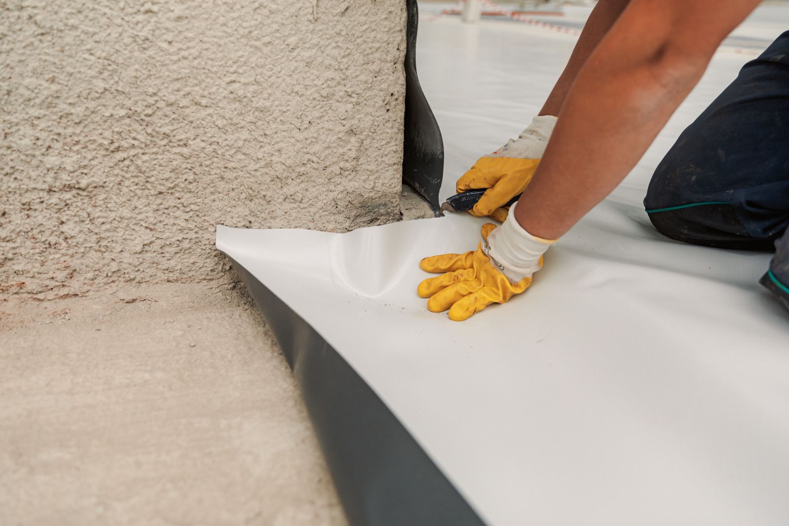 Person in yellow gloves applying a white waterproof membrane along a wall-floor corner