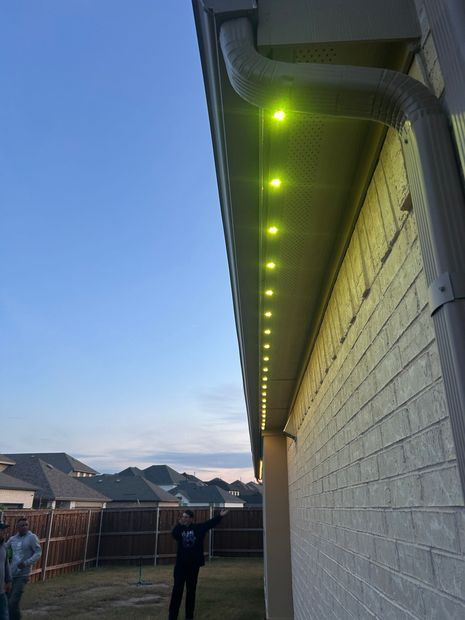 A man is standing in front of a house with yellow lights on the roof.