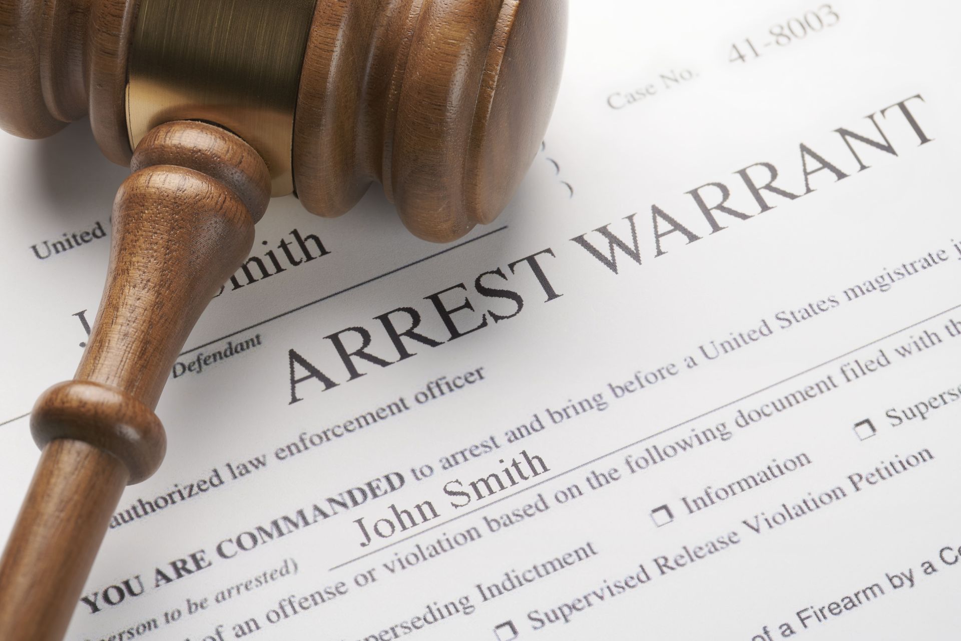 An arrest warrant document with a wooden gavel resting on top.