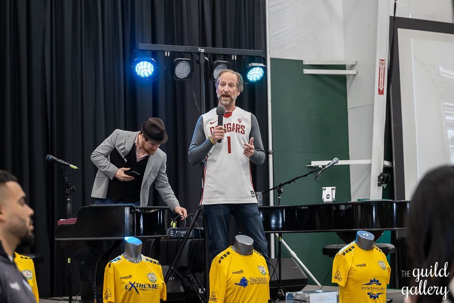 A man in a basketball jersey is standing in front of a microphone.