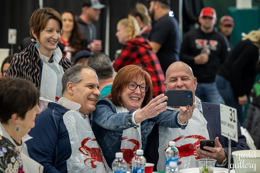 A group of people are sitting at a table taking a selfie with their cell phones.