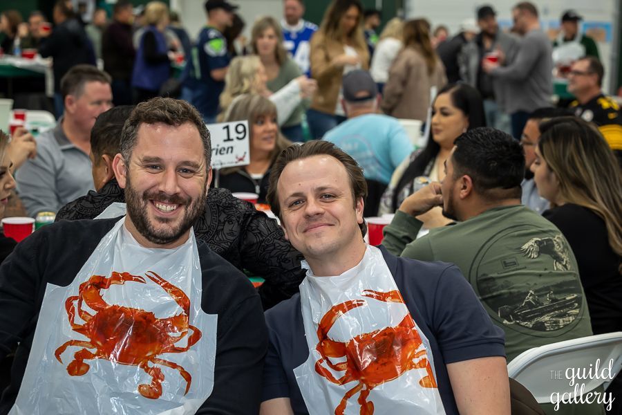 Two men wearing aprons with crabs on them are sitting at a table.
