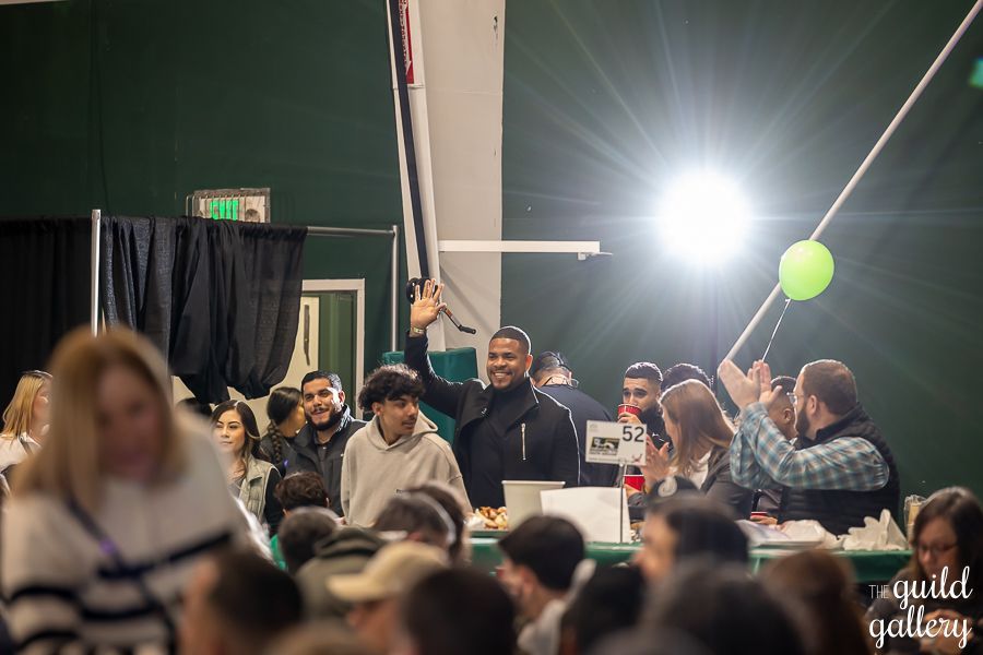 A man is standing in front of a crowd of people holding a green balloon.