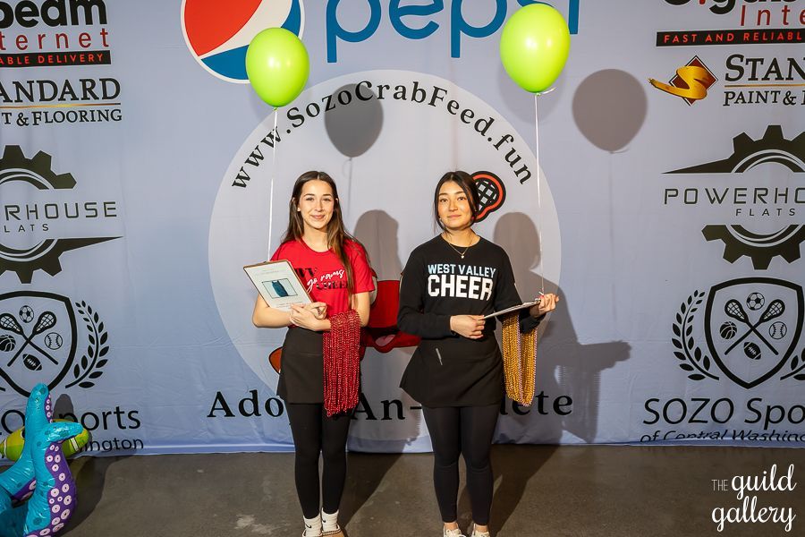 Two girls are standing in front of a pepsi sign