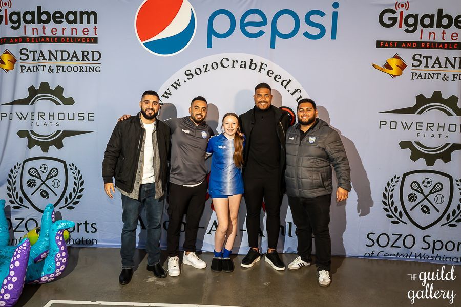 A group of people are posing for a picture in front of a pepsi sign.