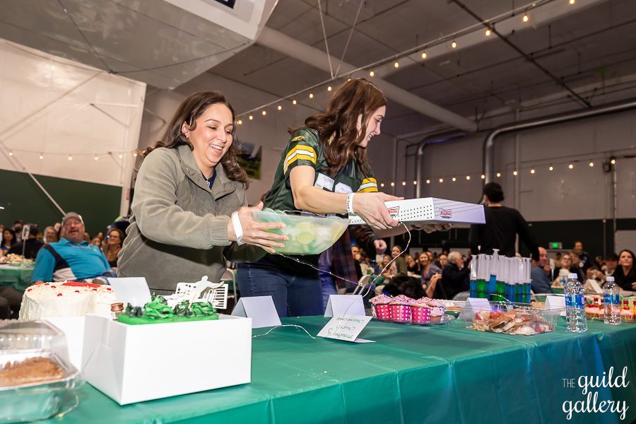 Two women are standing at a table with a bowl of food.
