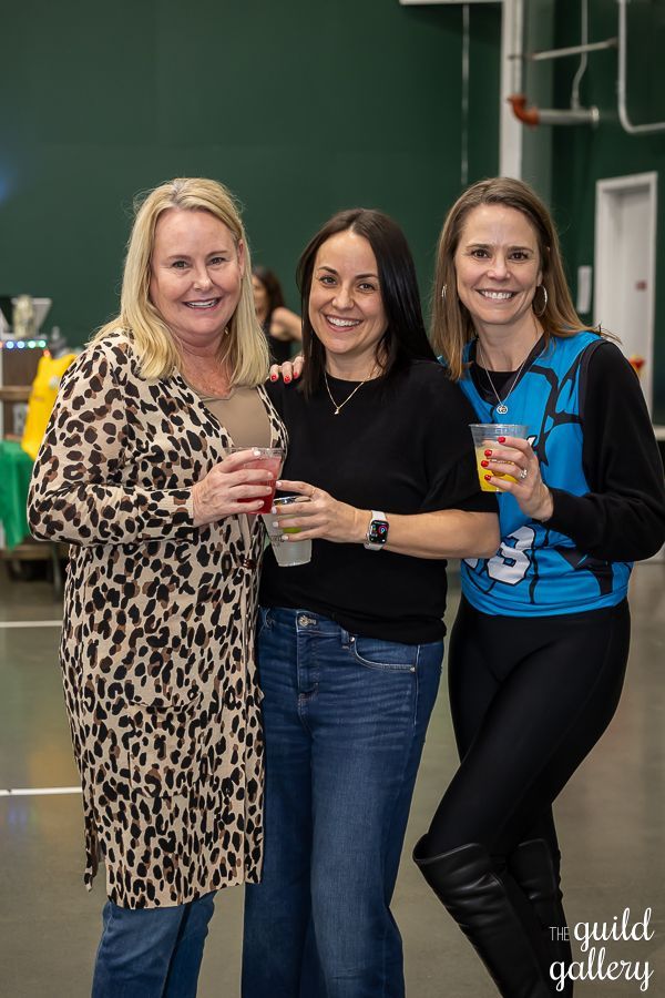 Three women are posing for a picture together while holding drinks.