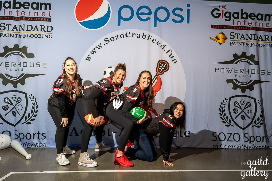 A group of women are posing for a picture in front of a pepsi banner.