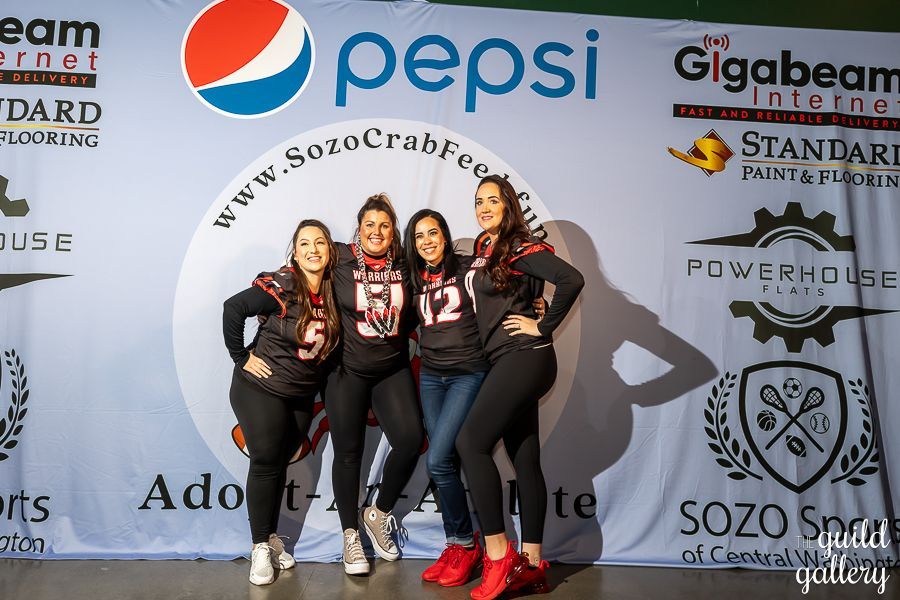 A group of women are posing for a picture in front of a pepsi banner.