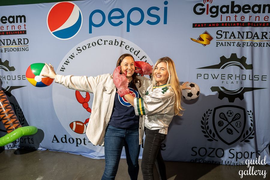 Two women are posing for a picture in front of a pepsi sign.