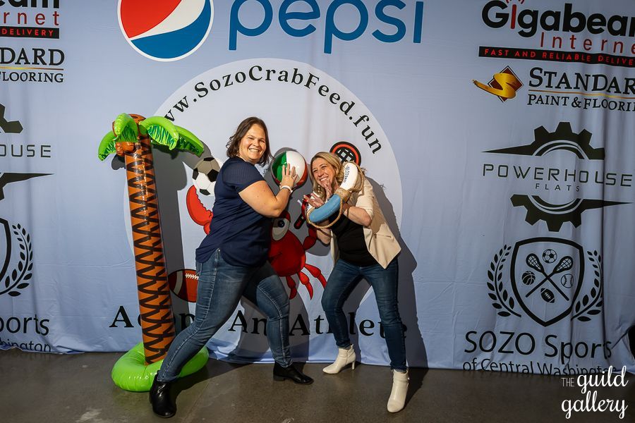 Two women are posing for a picture in front of a pepsi banner