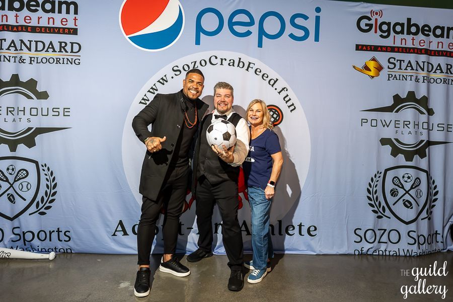 Three people are posing for a picture in front of a pepsi banner.