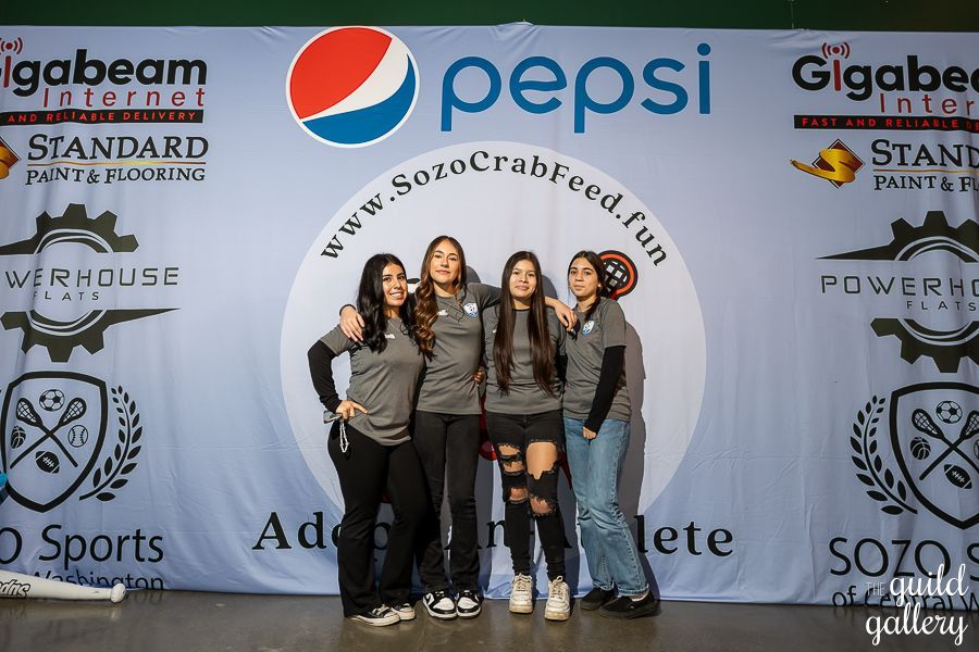 A group of women are posing for a picture in front of a pepsi sign.