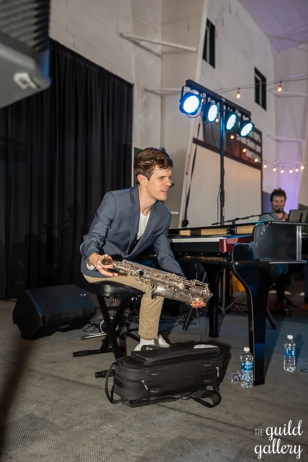 A man is sitting on a stool playing a saxophone on a stage.
