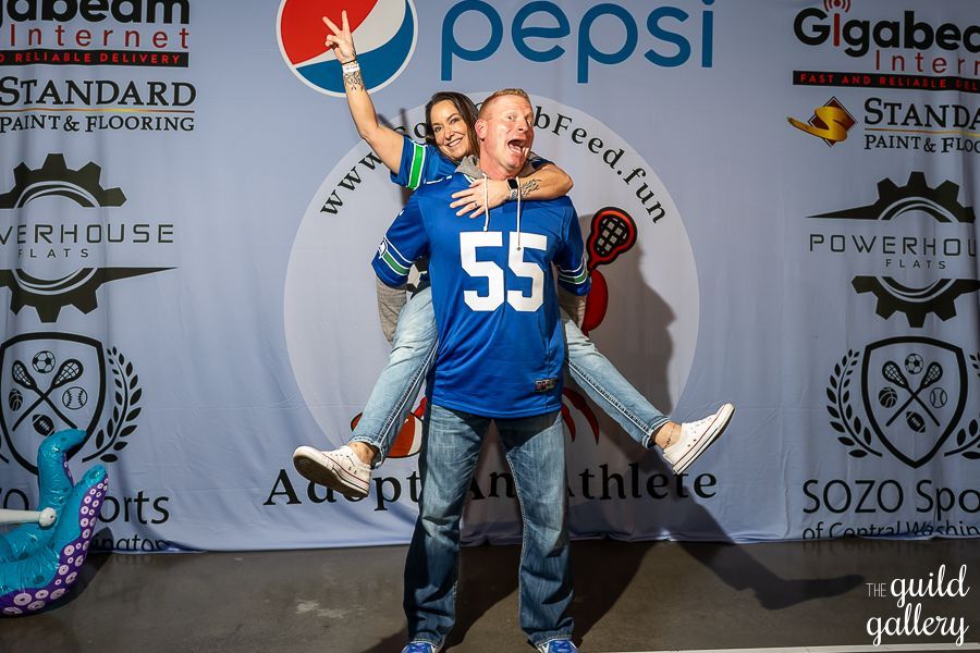 A man is carrying a woman on his shoulders in front of a pepsi banner