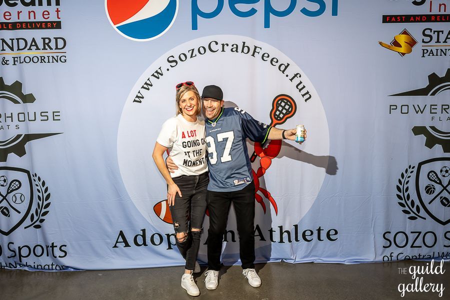 A man and a woman are posing for a picture in front of a pepsi banner.