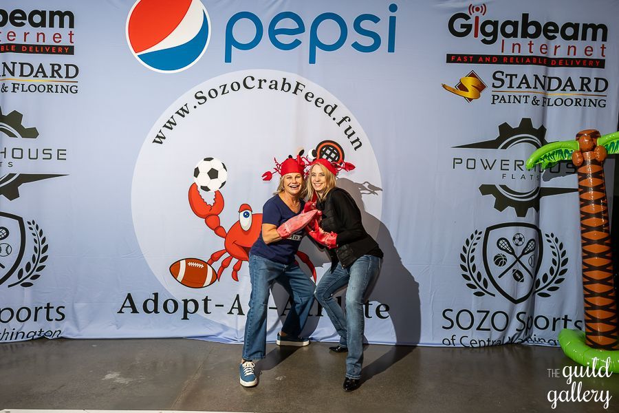 Two women pose in front of a pepsi sign