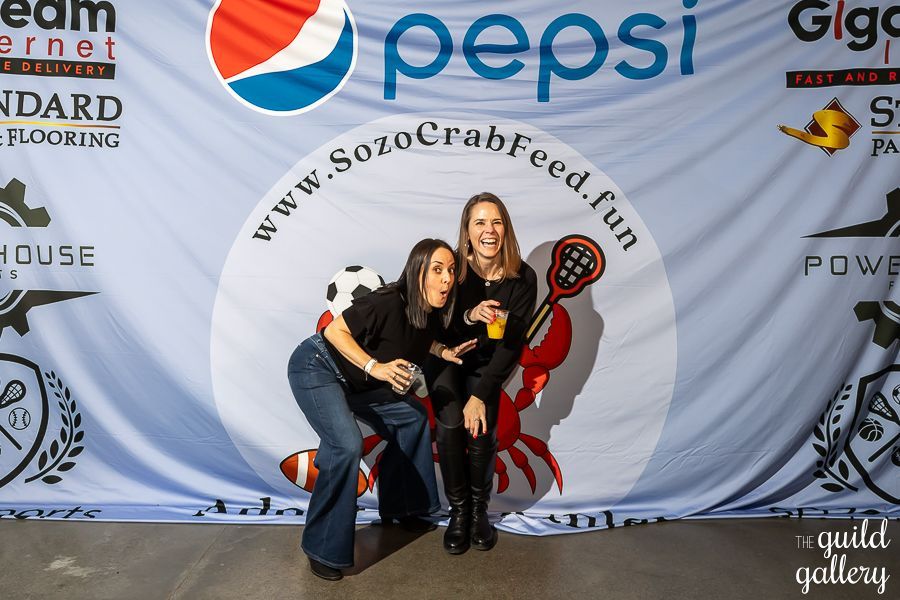 Two women pose in front of a pepsi banner