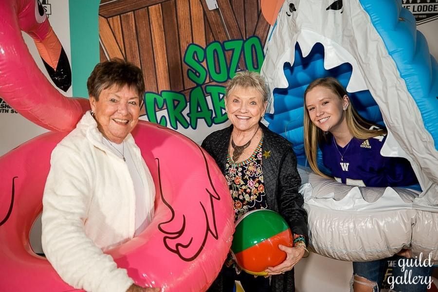 Three women are standing next to each other holding inflatable toys.