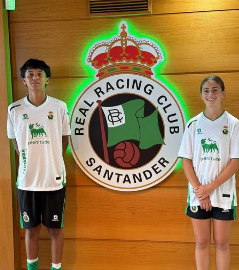 Two people in Real Racing Club jerseys pose in front of team logo.